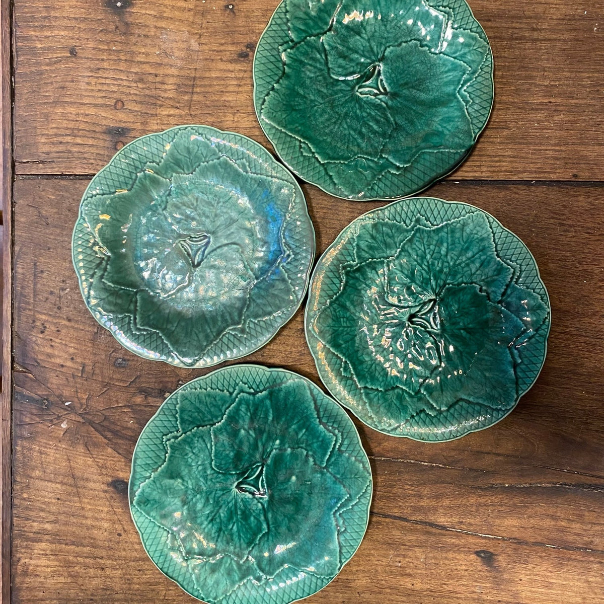 Fyra vintage Gien-tallrikar formade som blad, i något olika gröna nyanser, sedda ovanifrån på ett träbord