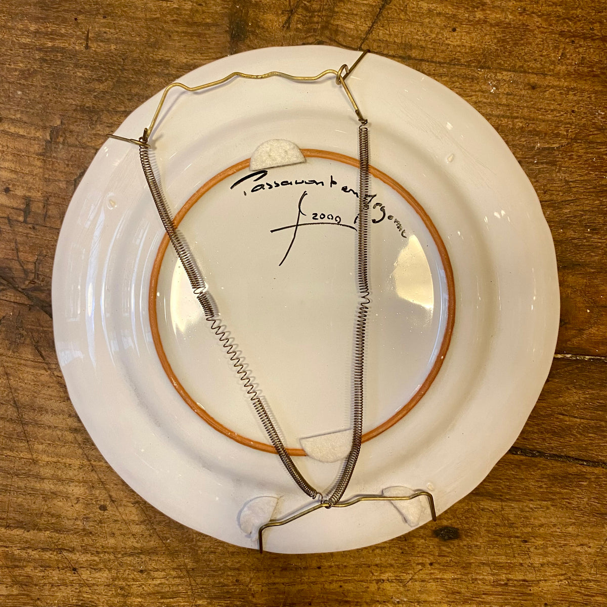 Baksidan av en vintage fransk väggtallrik med metallupphängning och en handskriven signatur