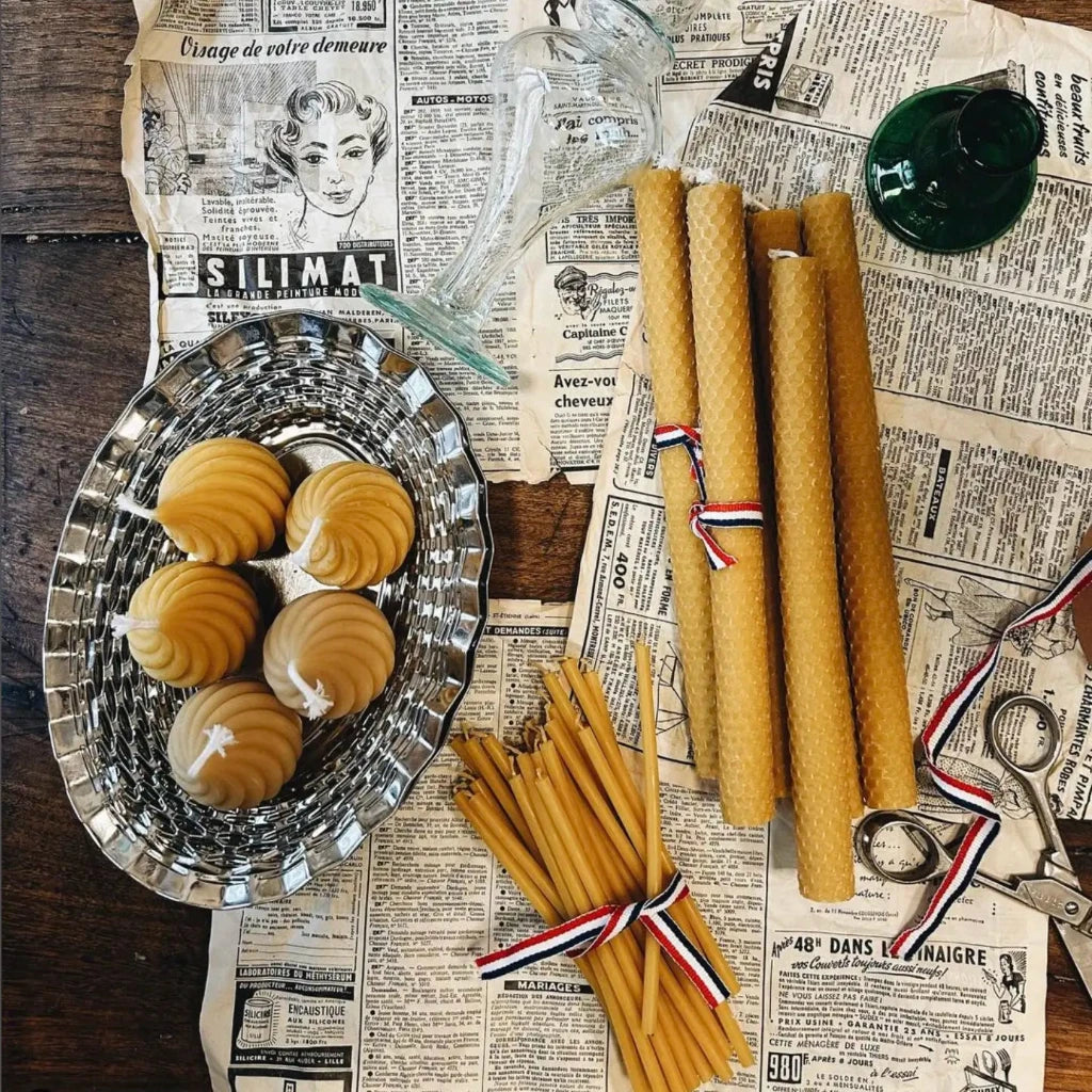 A picture of beeswax candles and glass objects in different shapes placed on an old french newspaper.