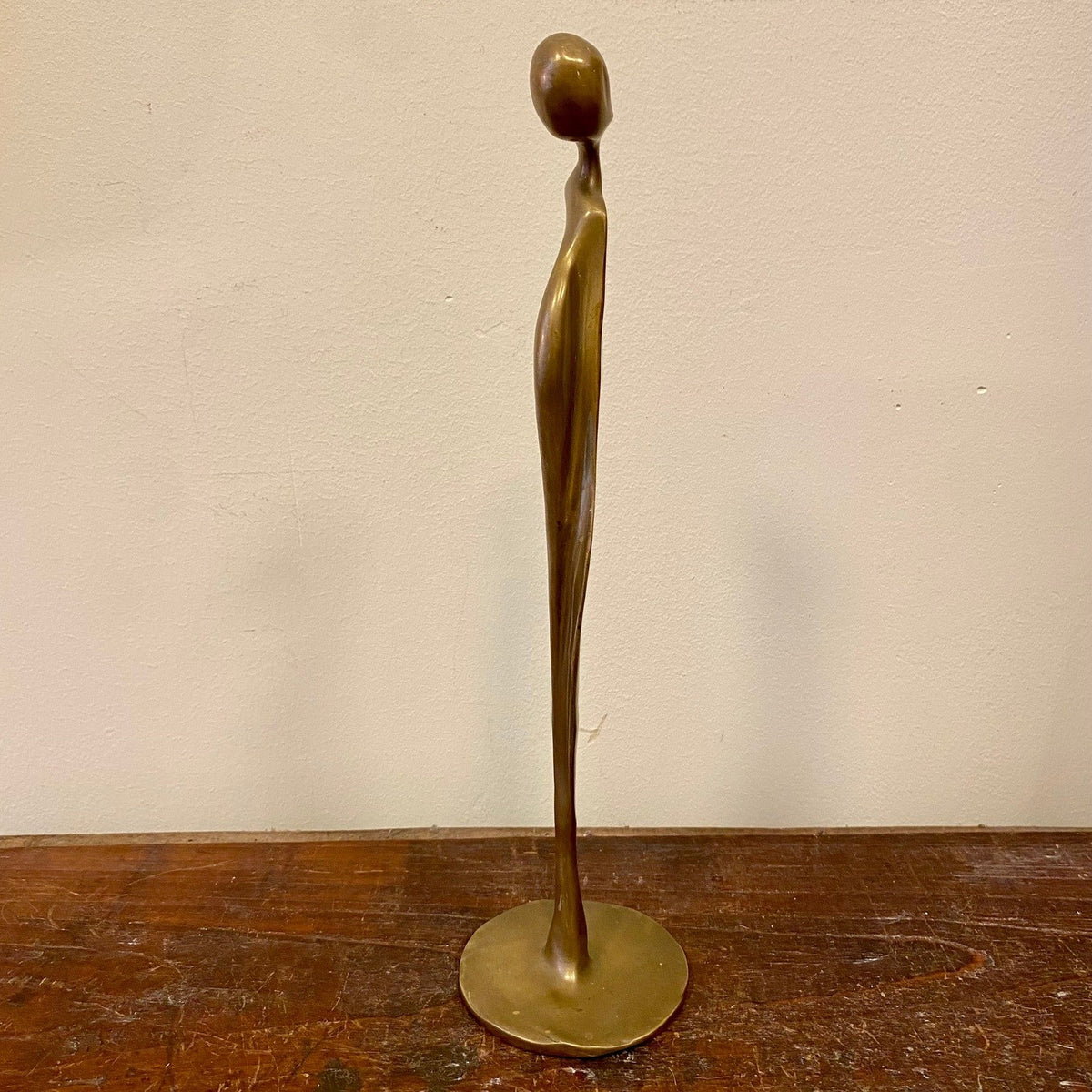 Abstrakt figur i mässing på rund bas, smal sidovy