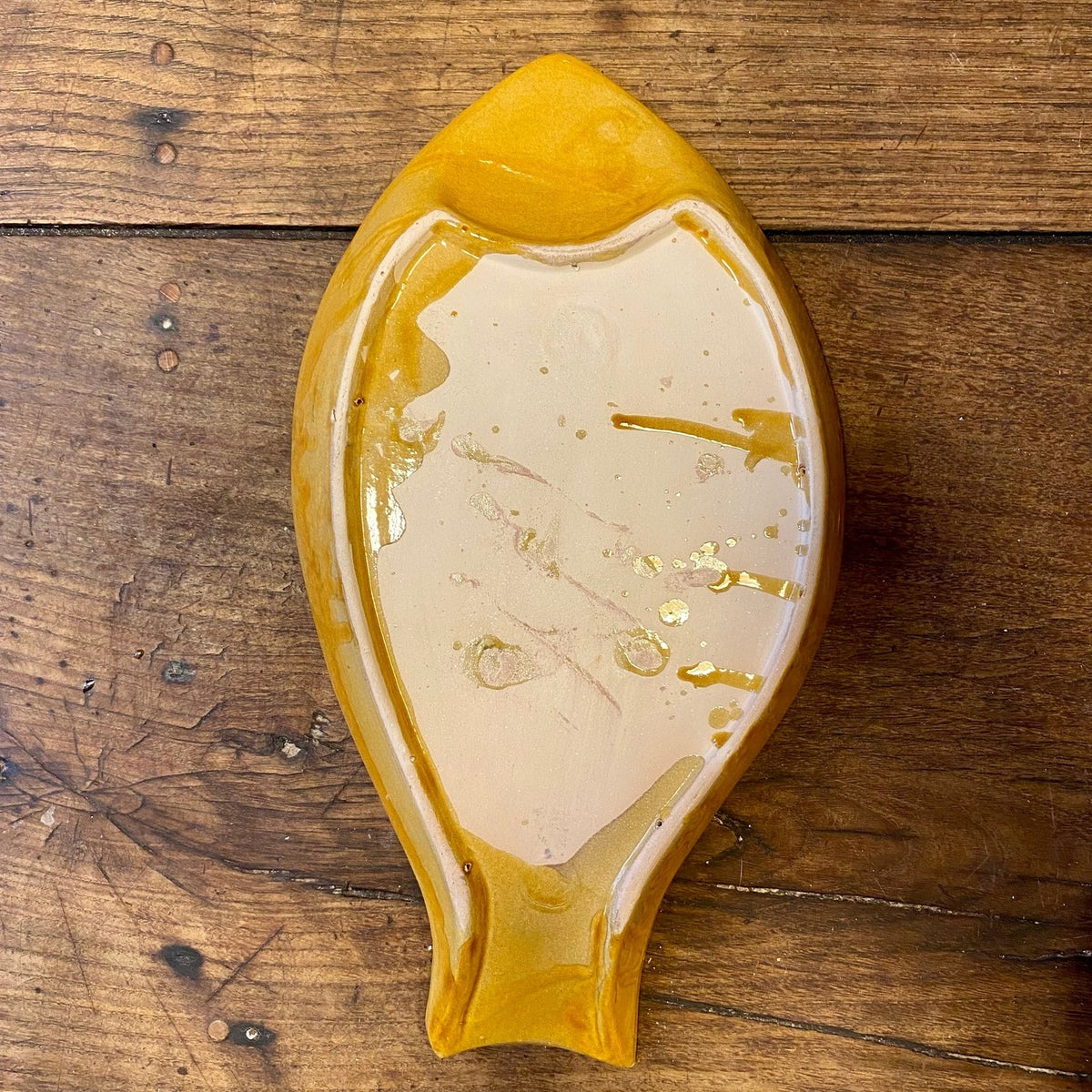 Underside of the fish-shaped dish with unglazed base and yellow glaze drips
