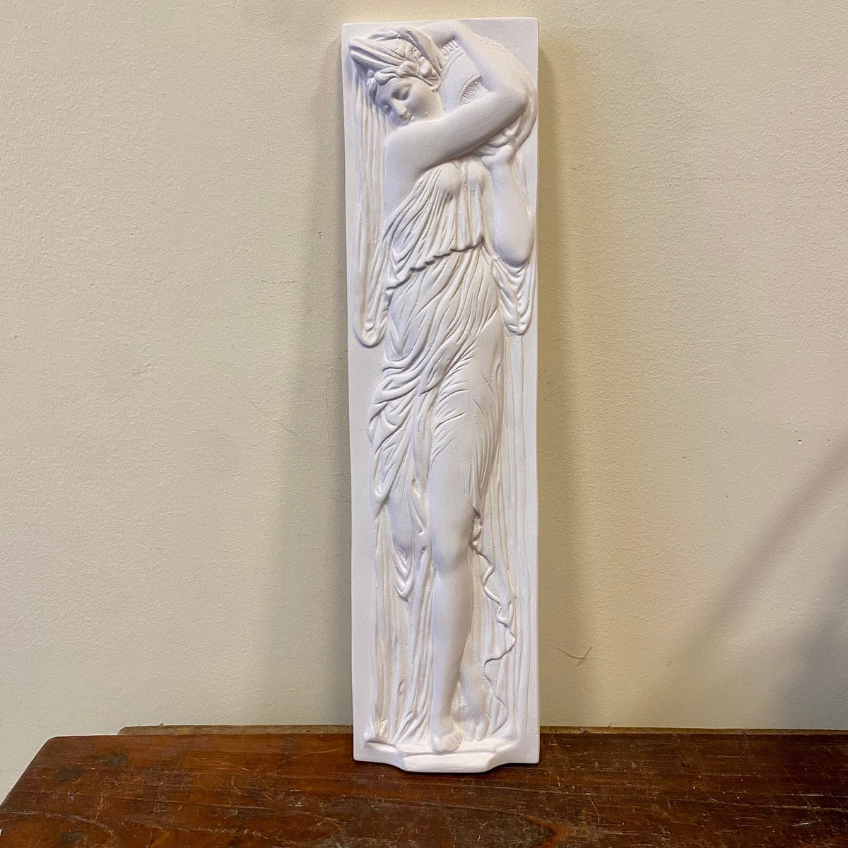 Plaster wall relief of a draped woman carrying an amphora, front view