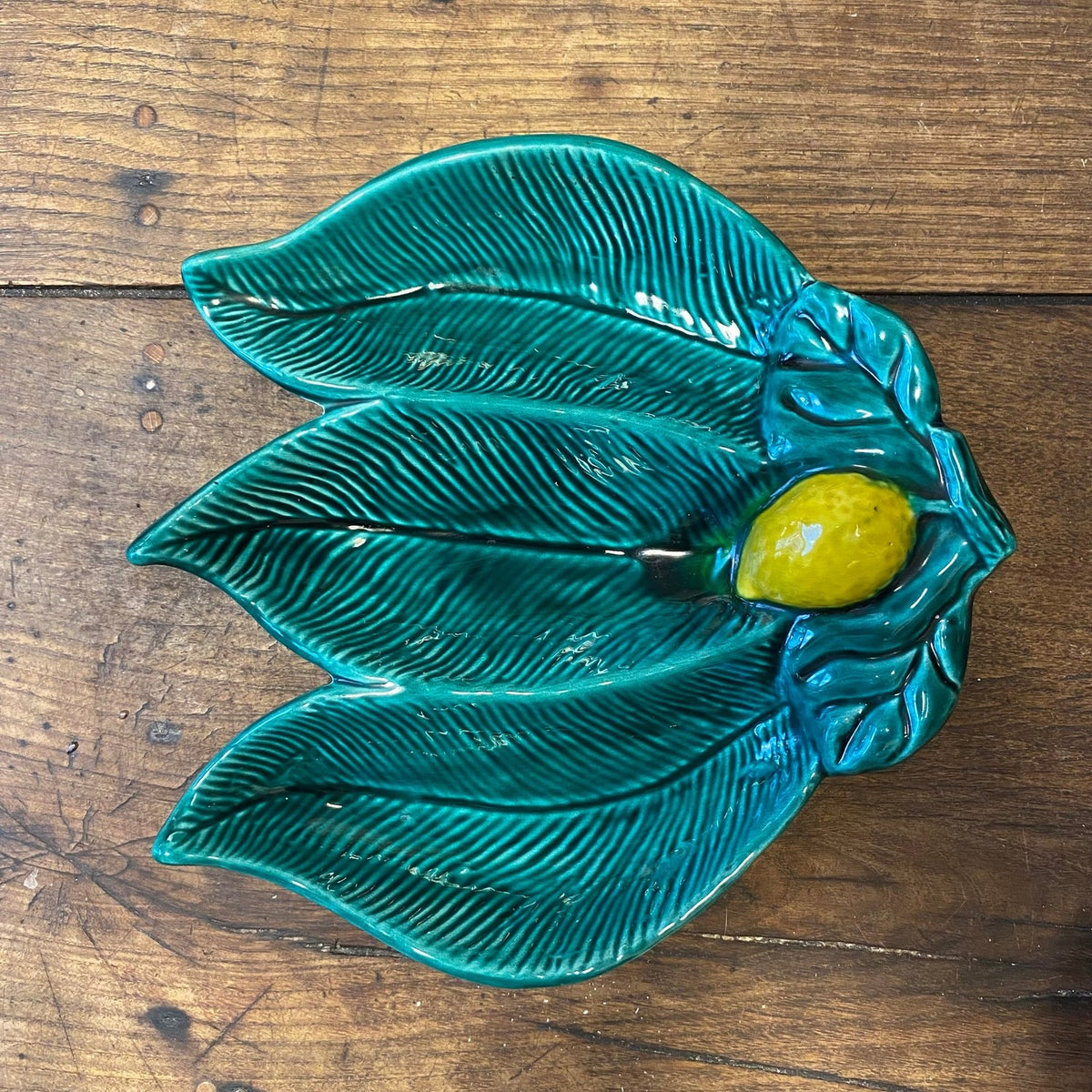 Green leaf-shaped Vallauris serving dish with a yellow lemon, seen from above