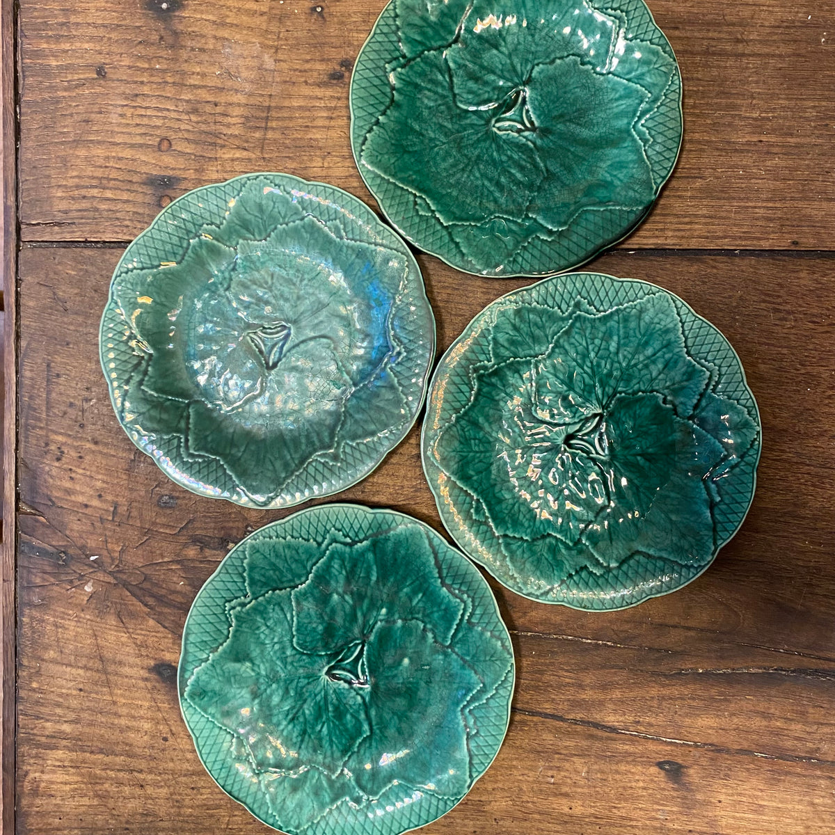 Four vintage Gien leaf plates in slightly different shades of green, seen from above on a wooden table