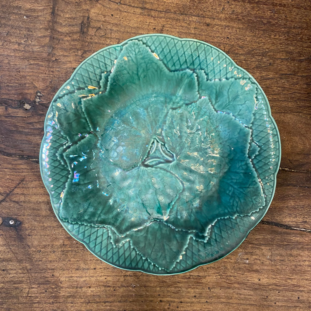 A paler, bluer green plate with iridescent patches in the glaze, with the same leaf design and lattice border