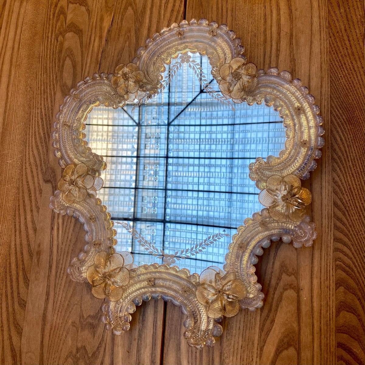 Vintage Venetian wall mirror with a scalloped glass frame and glass flowers, hanging on a wooden wall