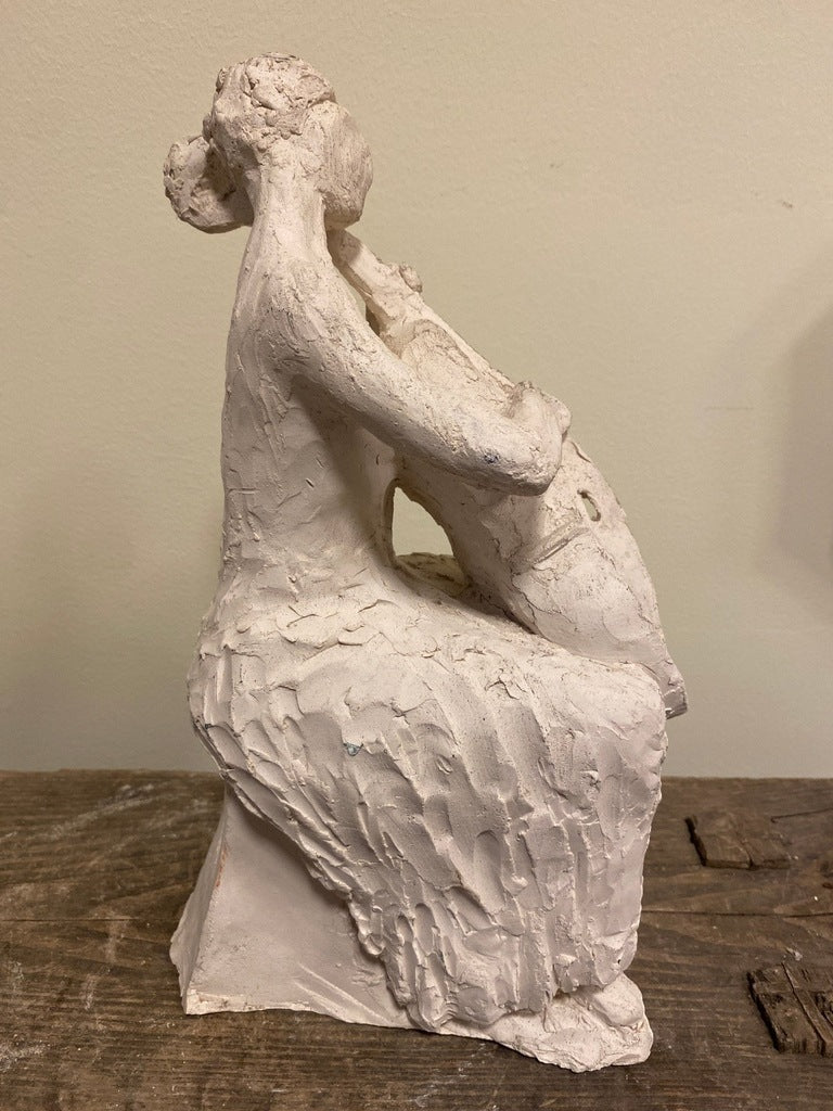 Sculpture of a seated figure playing a cello, side view.