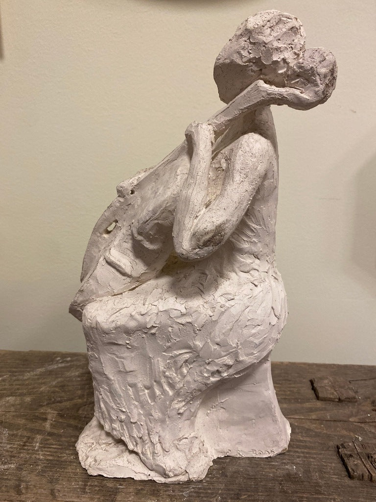 Sculpture of a seated figure playing a cello, side view.