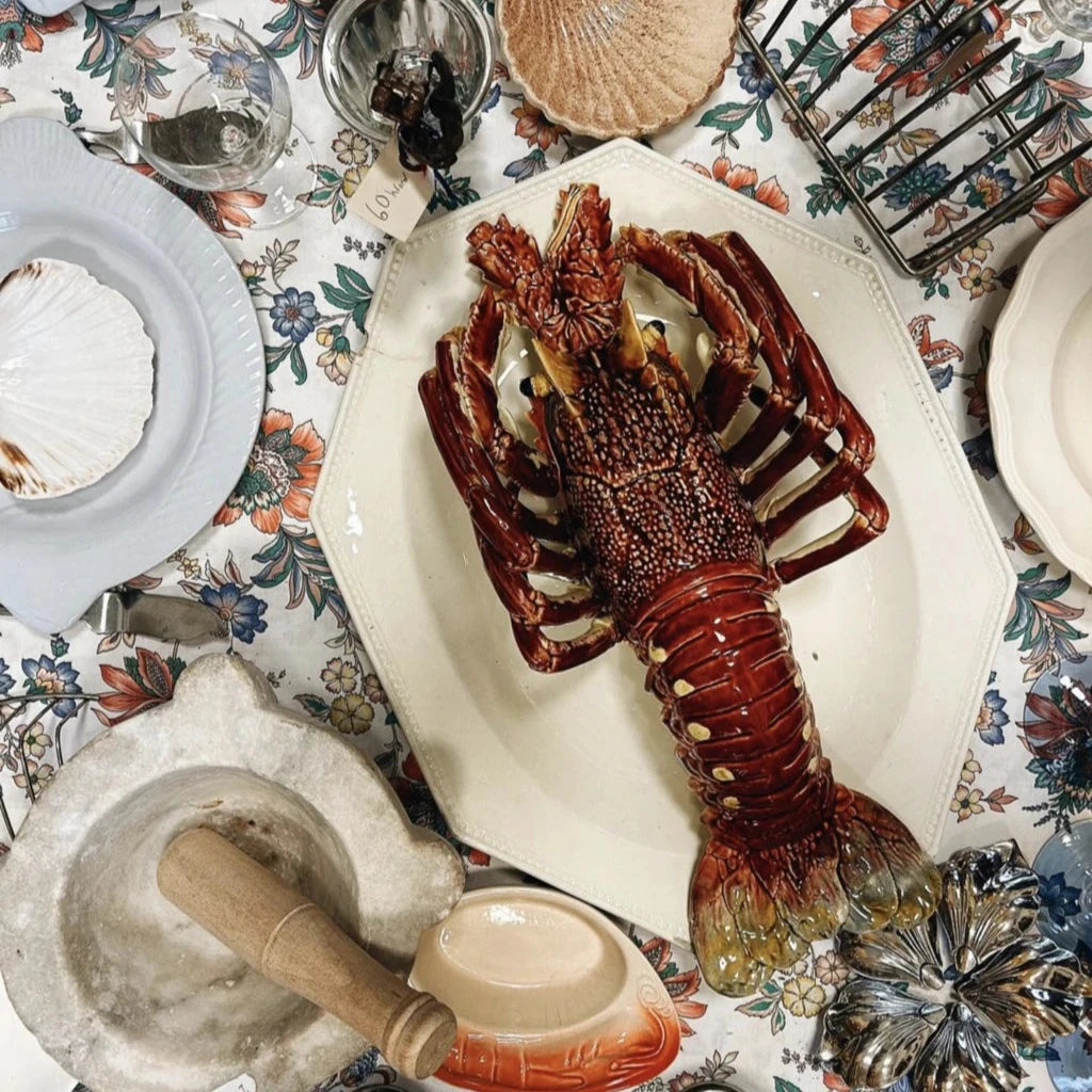 Colorful table setting with ceramic lobster centerpiece, seashell plates, and vintage glassware.