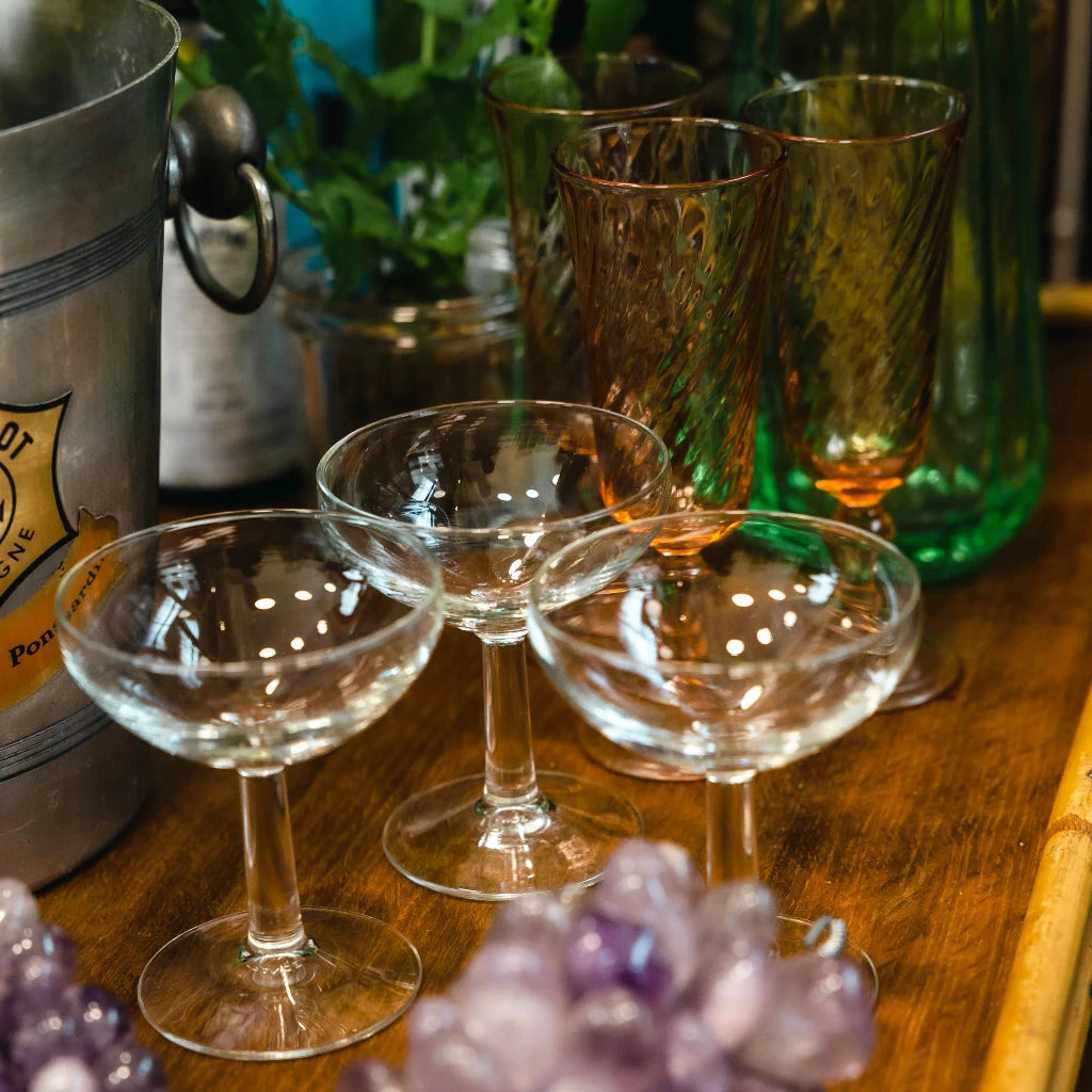 Elegant display of vintage glassware, including champagne coupes and colored glasses, with a wine cooler.