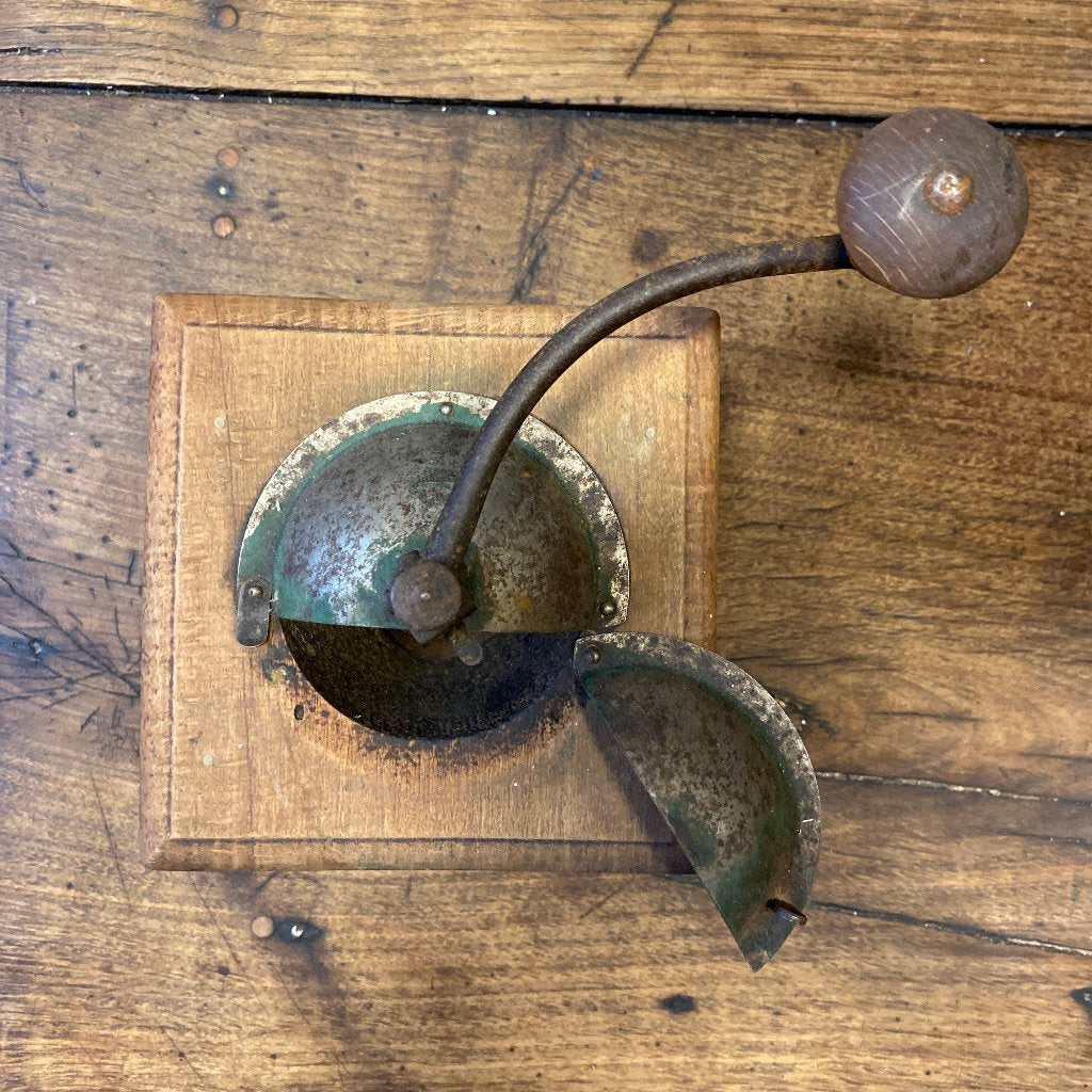 A vintage wooden pepper mill from above showing its rusty handle and cap.