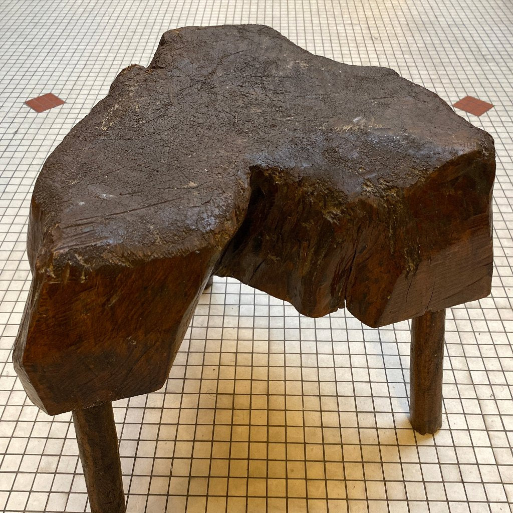 Old dark wooden stool. Made from a big tree trunk. 