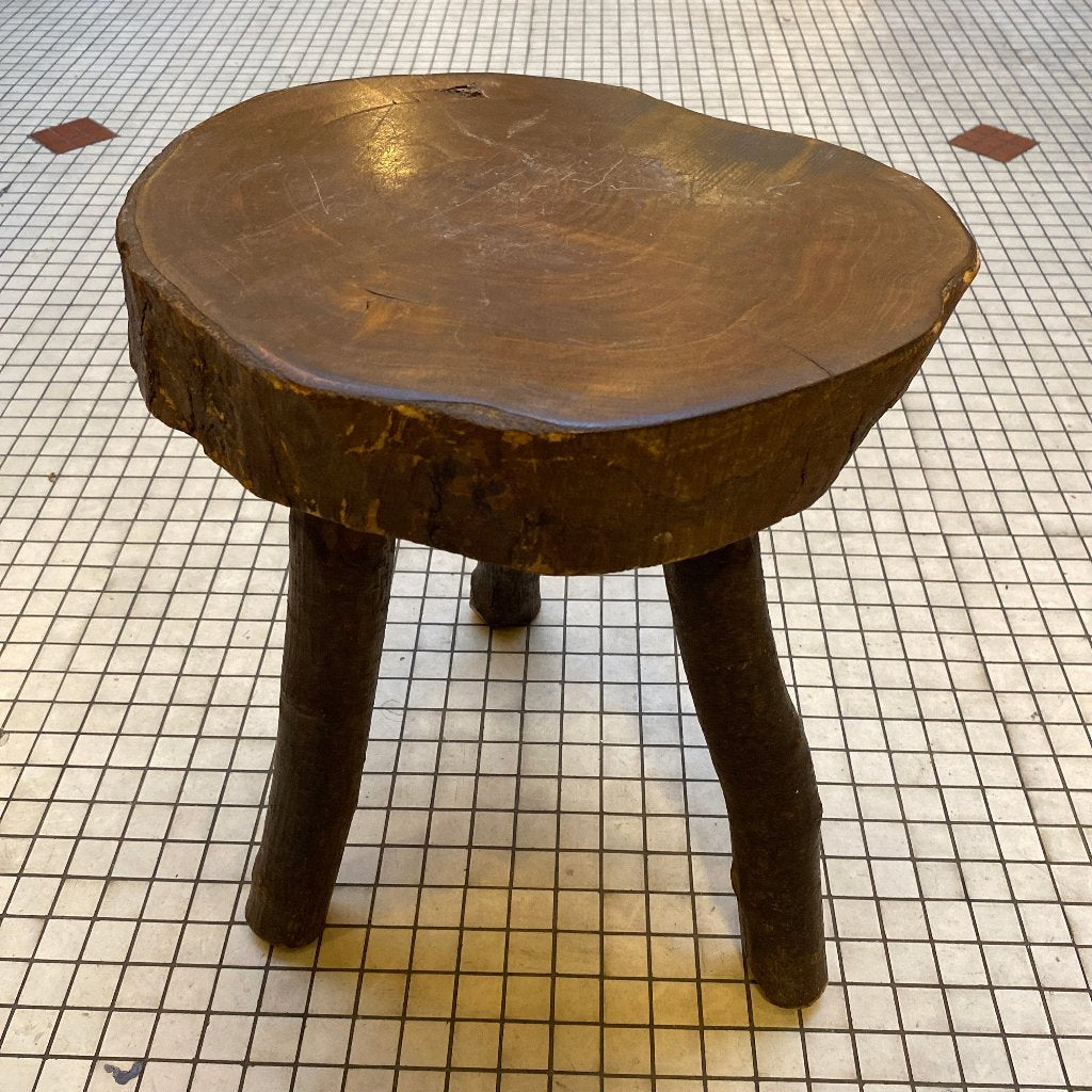 A wooden brutaliste stool. Tiled floor.